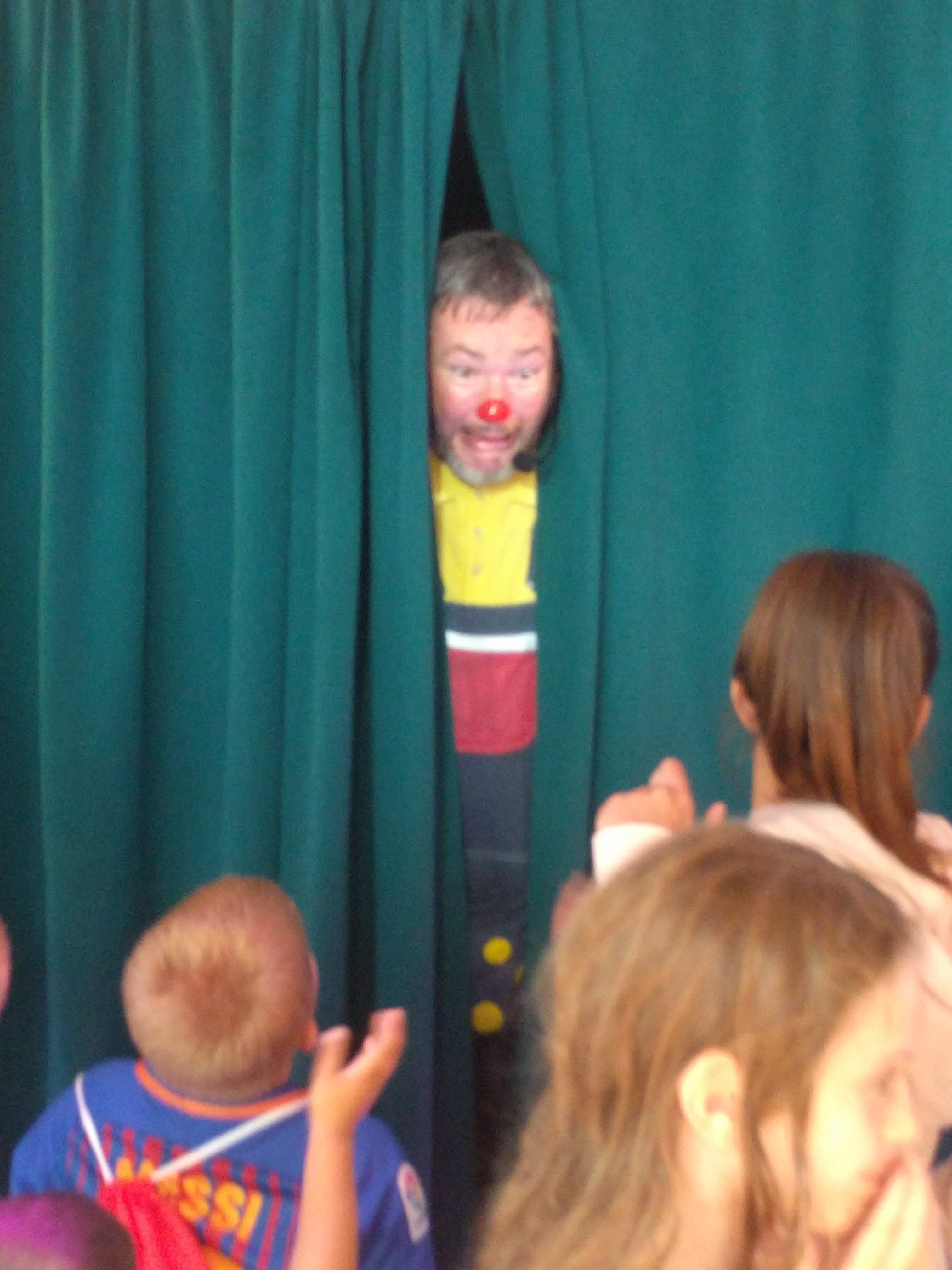 Curley Wurley Clown poking his nose through a stage curtain at some children